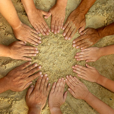hands in the sand in a circle signifying togetherness and teamwork